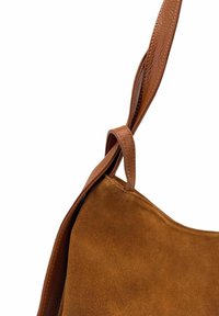 Sac à main en suede marron avec une sangle en cuir lisse, présentant un détail en nœud. Le sac a une texture douce et une forme simple et courbée.
