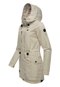 Beige vattentät jacka med huva, dragsko i midjan, ficka med dragkedja framtill och två fickor med klaff, med svarta detaljer.