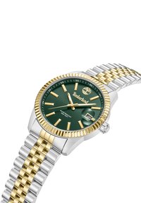 Orologio con quadrante verde, cinturino in acciaio inossidabile e tonalità oro, caratterizzato da una lunetta testurizzata, indici delle ore dorati e finestra per la visualizzazione della data.