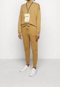 Brauner, weicher Sweatshirt mit hohem Kragen und lässiger Passform. Passende, schmal zulaufende Sweatpants mit Kordelzug. Weiße Sneakers runden das Outfit ab.