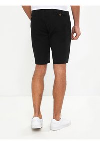 Bermudas de algodón negras con un diseño ajustado, que cuentan con bolsillos y un detalle de botón en la parte posterior. Llevadas con zapatillas blancas.