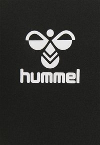 Tela negra con un logotipo blanco prominente que presenta un diseño simétrico de dos alas y una forma central, acompañado de la palabra "hummel."