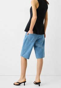 Svart, ärmlös topp med ribbat mönster; ljusblå denimshorts som når till mitten av låret, med bakfickor och avslappnad passform; svarta klacksandaler.