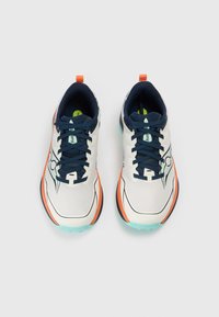 Chaussures de course avec une tige légère en mesh blanc, lacets bleu marine et accents orange. La semelle présente une base turquoise avec un motif texturé.