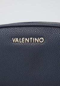Borsa a mano in pelle blu navy con superficie testurizzata, caratterizzata dal logo dorato "VALENTINO". Chiusura con zip sulla parte superiore e foderatura in tessuto morbido.