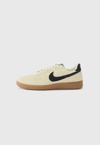Lysegule ruskind sneakers med sort swoosh-logo, flade snørebånd og brun gummisål. Klassisk low-top design. Struktureret materiale.