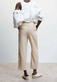 Lichtbeige cropped broek, elastische tailleband, achterzakken, gecombineerd met een losvallend wit linnen shirt en beige sneakers met zwarte accenten.