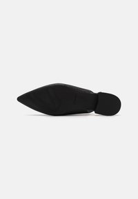 Chaussure noire à bout pointu avec un upper texturé et une semelle en caoutchouc lisse. Présente un branding subtil sur la semelle et une silhouette élégante.