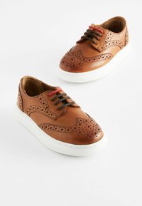 Chaussures en cuir marron avec des détails en brogue, bout rond et semelle en caoutchouc blanche. Équipées de lacets rouges et noirs pour un intérêt de design supplémentaire.