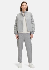 Grijs cropped jack met staande kraag, drukknoopsluiting, elastische manchetten; gecombineerd met grijze broek en witte sneakers, met een geribde trui.