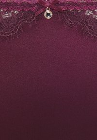 Tief violetter Stoff mit Spitzenbesatz entlang der oberen Kante und einer kleinen Schleife in der Mitte, die einen runden klaren Edelstein-Anhänger zeigt.