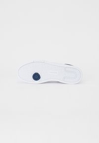Fehér sneaker talp textúrált mintával, kör alakú sötétkék akcentussal és márkajelzéssel. Simább felület lapos formával.