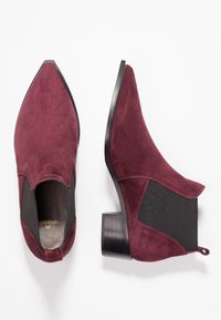 Burgundy suede ankle boots with a pointed toe, elastic side panels, and a chunky black heel. Smooth texture with minimal stitching details.