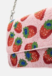 Koristeltu käsilaukku vaaleanpunaisella pohjalla, jossa on mansikkakuvio punaisena, vihreänä ja sinisenä. Ketjuhihna ja läppäsuljenta tuovat lisäyksityiskohtia.