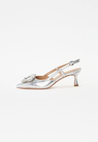 Zapato de slingback metálico plateado con punta afilada, que presenta una decoración floral y un tacón bajo, en bloque. Correas delgadas añaden detalle.