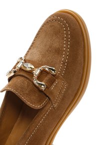 Braune Wildleder-Loafer mit runder Spitze, ausgestattet mit dekorativer goldfarbener Hardware und kontrastierenden Nähten entlang des Vorderfußes und der Sohle.