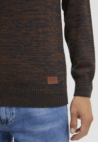 Maglione lavorato a maglia in blu scuro e arancione con un motivo testurizzato. Presenta polsini a coste e una piccola etichetta marrone del marchio in basso.