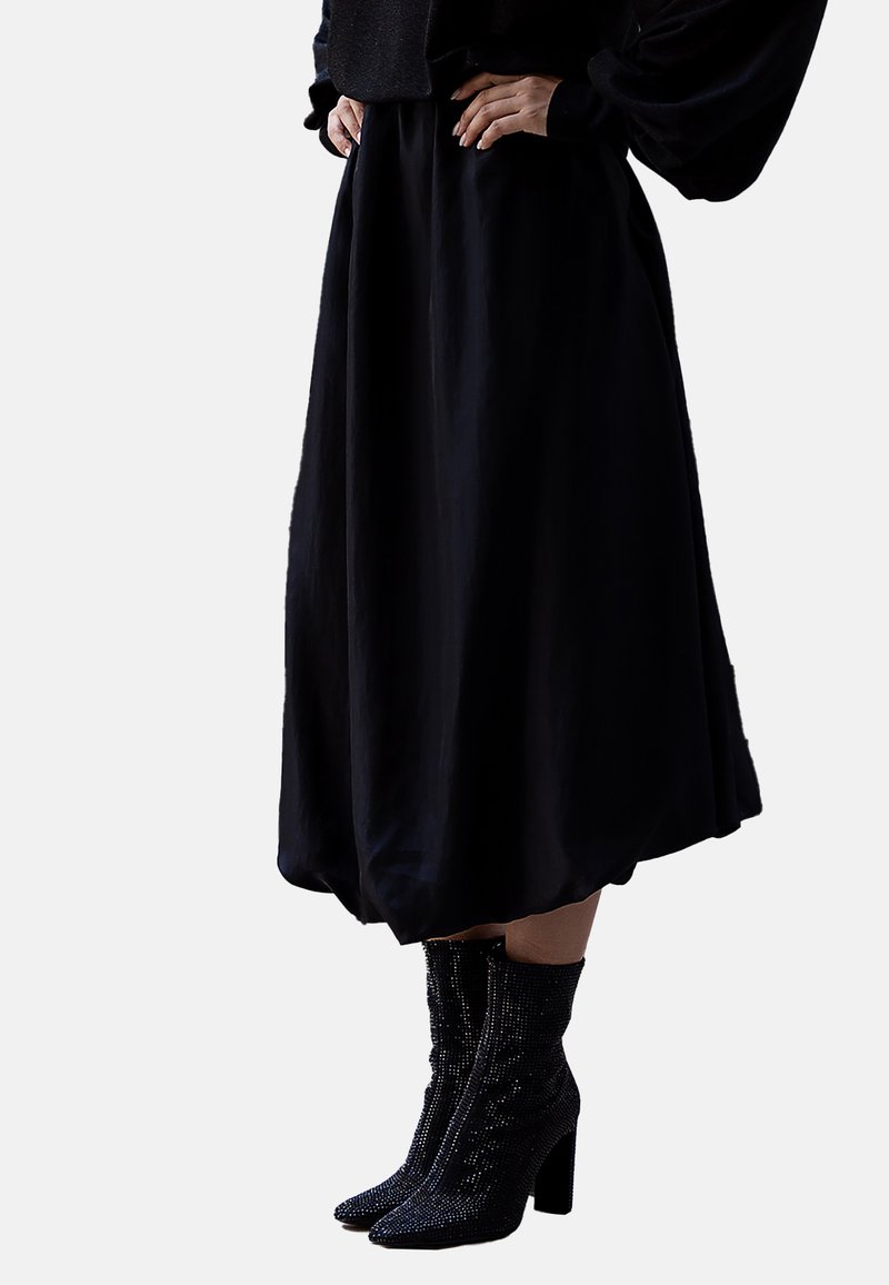 Schwarzer knielanger Rock mit fließender Silhouette aus leichtem Stoff. Kombiniert mit glitzernden schwarzen Stiefeletten mit einem klobigen Absatz.