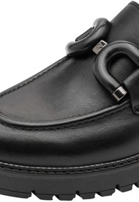 Mocassin en cuir noir avec semelle en caoutchouc épaisse et boucle métallique noire brillante décorative sur la partie avant supérieure.