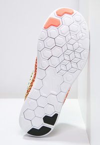 Sole obuvi s bílým gumovým povrchem a hexagonálními vzory, doplněný oranžovými a černými detaily, navržený pro trakci a flexibilitu.