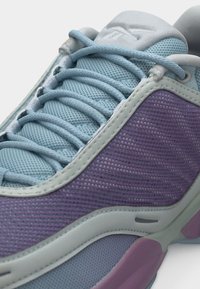 Μωβ και ανοιχτό μπλε αθλητικό παπούτσι με ύφασμα από δίχτυ, ανοιχτό μπλε κορδόνια και λευκές λεπτομέρειες περιγράμματος πάνω σε λευκό φόντο.