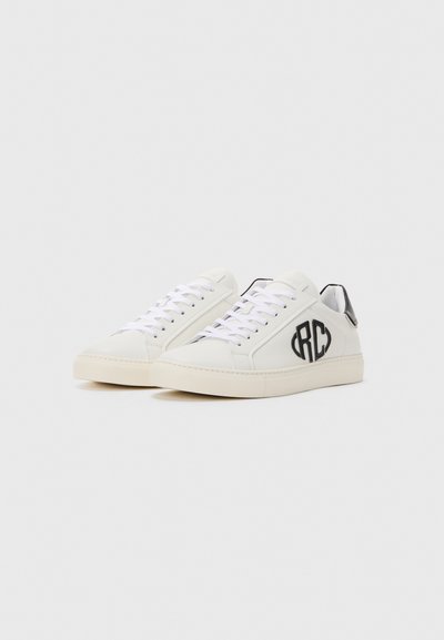 White low-top sneakers with black "RC" logo on side, white laces, and black heel tab, displayed on a plain light background.