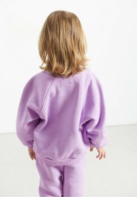 Fioletowy sweatshirt i dopasowane spodnie z miękkiej tkaniny o luźnym kroju, z ribbowanymi mankietami i paskiem, widziane z tyłu.