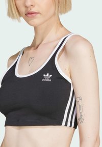 Zwarte sportbeha met witte afwerking, voorzien van een ronde halslijn en dunne bandjes. Adidas-logo aan de voorkant. Zachte stoftextuur.