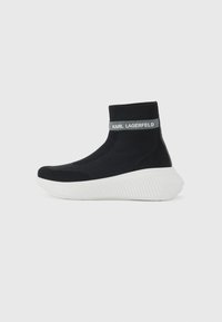 Knit black ankle sneaker with a ribbed collar, white textured sole, and branded grey accent. Features a streamlined, sock-like design.