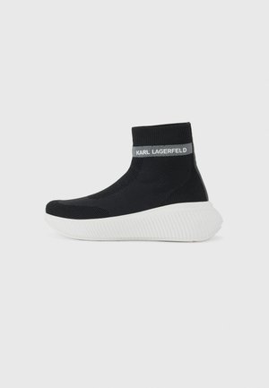 Knit black ankle sneaker with a ribbed collar, white textured sole, and branded grey accent. Features a streamlined, sock-like design.