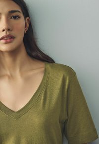 Olijfgroen V-hals T-shirt van zacht, lichtgewicht materiaal met korte mouwen en subtiele stikdetails op de halslijn en de mouwen.