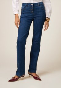 Jeans din denim albastru închis, cu croială dreaptă și talie înaltă, având patru butoane și buzunare frontale. Asortate cu tocuri din piele lăcuită burgundă.