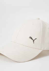 Hvid baseballcap med et struktureret stof, prydet med et metallisk Puma-logo foran. Bøjet skygge med synlige syninger.