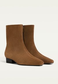 Smeđi nubuk čizmi do članaka s uskim vrhom, glatkom teksturom, bočnim zatvaračem i niskim blok petom, koji predstavljaju elegantan i usklađen oblik.