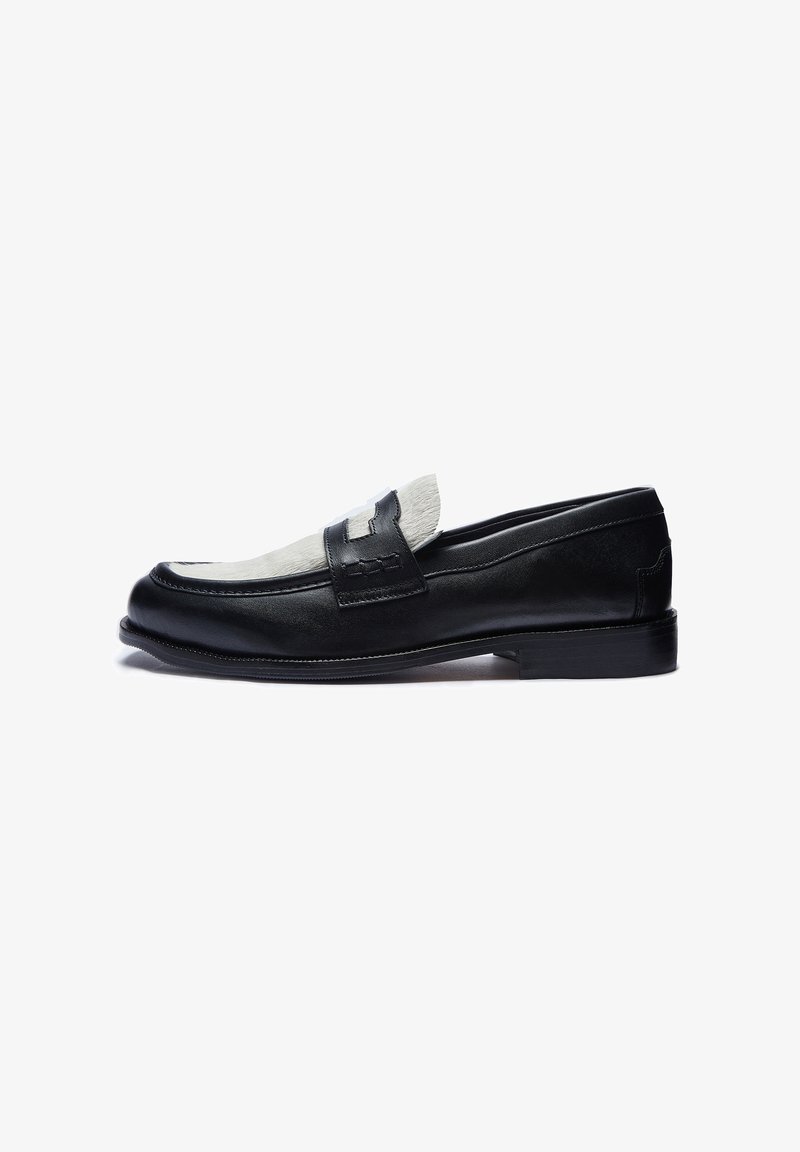 Mocassin en cuir noir avec panneau supérieur en fourrure blanche et détail de bride décorative, talon bas, présenté de profil sur fond blanc.