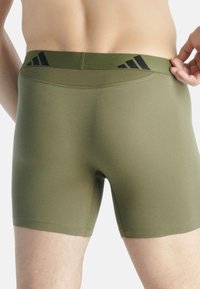 Boxer-briefs vert olive en matériau extensible avec une texture lisse. Présente un logo noir sur la ceinture et un design ajusté.