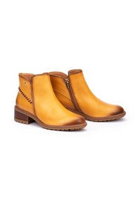 Botas de tobillo de cuero amarillo con punta redondeada, tacón marrón, cremallera lateral y costuras decorativas en el lado exterior. Suela de goma texturizada.