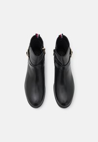 Botas de tobillo de cuero negro con un diseño elegante, que presentan un acento de hebilla dorada y un acerico a rayas. Textura suave y punta afilada.