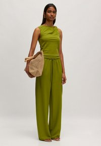 Groene mouwloze top en set met wijde broek, met een geweven tas met trekkoord, staande tegen een neutrale achtergrond.