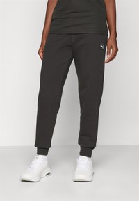 Schwarze Pullover-Jogginghosen mit schmal zulaufendem Bein, gerippten Bündchen und einem kleinen weißen Logo-Patch an der Hüfte. Hergestellt aus weichem, strukturiertem Stoff.