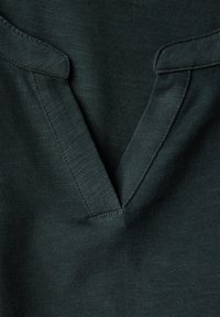 Tummanvihreä neulepusero, jossa on V-kaula-aukko ja litteät ommellut reunat. Kangas on sileä ja siinä on hieno höttökuvio.