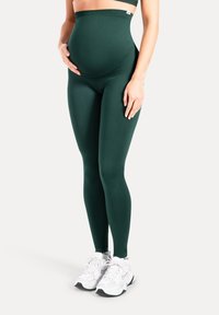 Gröna leggings med hög midja i mjukt, stretchigt tyg, designade för komfort under graviditeten, kombinerade med vita sportskor.
