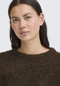 Maglione marrone con trama, collo rotondo e materiale morbido e peloso, caratterizzato da una vestibilità ampia e un design minimalista.