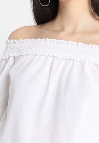 Top bianco scollato sulle spalle con scollatura arricciata, realizzato in tessuto di lino leggero, con una vestibilità comoda e una sottile texture.