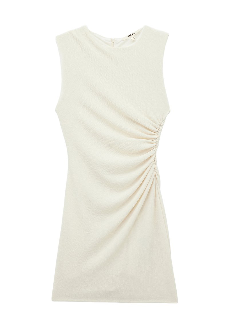 Haut sans manches beige clair en tissu texturé, avec un gathering asymétrique à l'avant et une fermeture éclair dissimulée à l'arrière.
