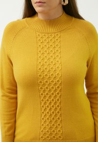 Maglione giallo lavorato a maglia con un collo alto a coste e un pannello centrale testurizzato con un motivo geometrico, maniche definite e orlo.