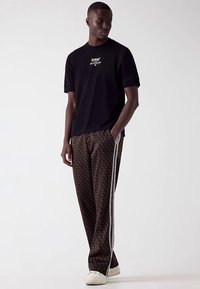 Black t-shirt with logo, paired with brown patterned pants featuring white side stripes and white sneakers. Simple, casual design.