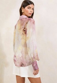 Doorzichtige blouse in pastelroze tinten met bloemen- en slangenprint; lange mouwen met textuurmanchet en knoopdetail.