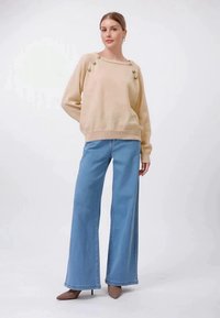 Camisola bege de malha com botões no decote, combinada com jeans de perna larga azul claro e sapatos altos castanhos.