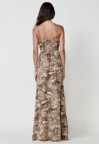 Brown maxi dress with spaghetti straps, gathered bodice, and a patterned fabric featuring abstract shapes and textures. Adjustable straps.